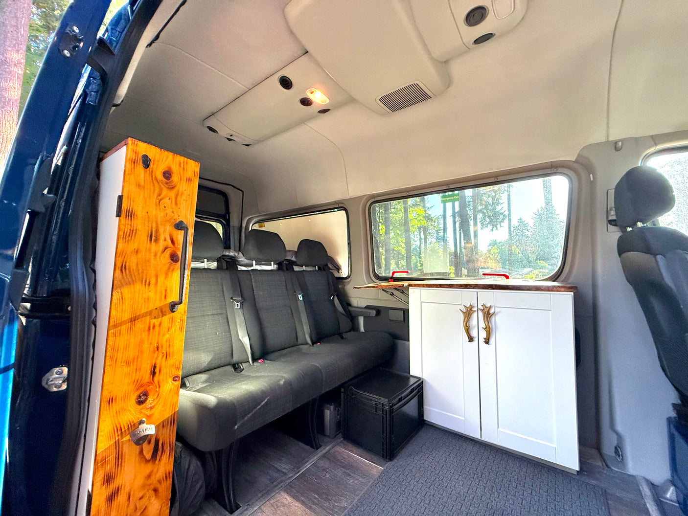 Experience comfortable **rv rental** travel in this spacious camper van, featuring custom wood cabinets, bench seating, and scenic outdoor views.