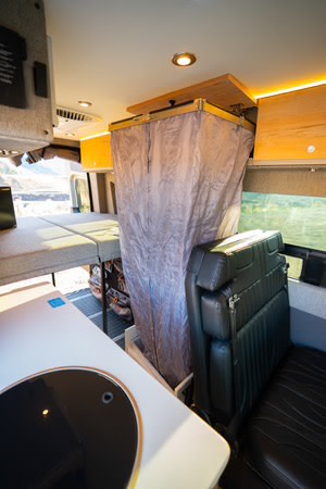 Inside our rv rental: a compact interior featuring a versatile portable shower/storage unit, kitchen, and convertible bed.