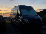 Coastal RV rental Sprinter van at sunset. Dark van silhouetted against a vibrant orange and blue ocean horizon.