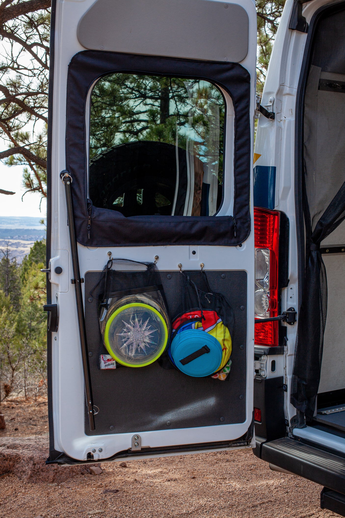 Maximize space in your RV rental! Rear van door with mesh storage bags holding discs and gear, parked in a scenic outdoor setting.