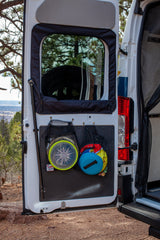 Maximize space in your RV rental! Rear van door with mesh storage bags holding discs and gear, parked in a scenic outdoor setting.