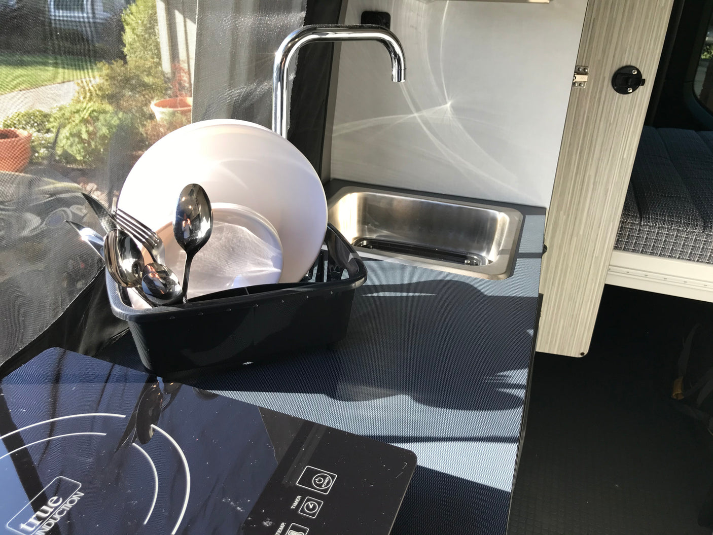 Enjoy an RV rental's functional mobile kitchen with induction cooktop, sink, and dish drying rack for convenient camping.