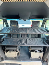 Inside an RV rental van, a black Patented Cabbunk creates a two-tier bunk over the front seats for sleeping or storage.