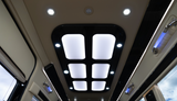 RV rental interior: Modern ceiling with bright panel and spot lighting, plus blue accent grab handles.