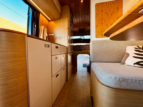 Bright RV rental interior: modern kitchenette with sink, pull-out drawers, cozy seating, and warm wooden ceilings.