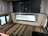Inside an RV rental: nature-patterned cushions, pop-top walls, and a window for scenic camping views.