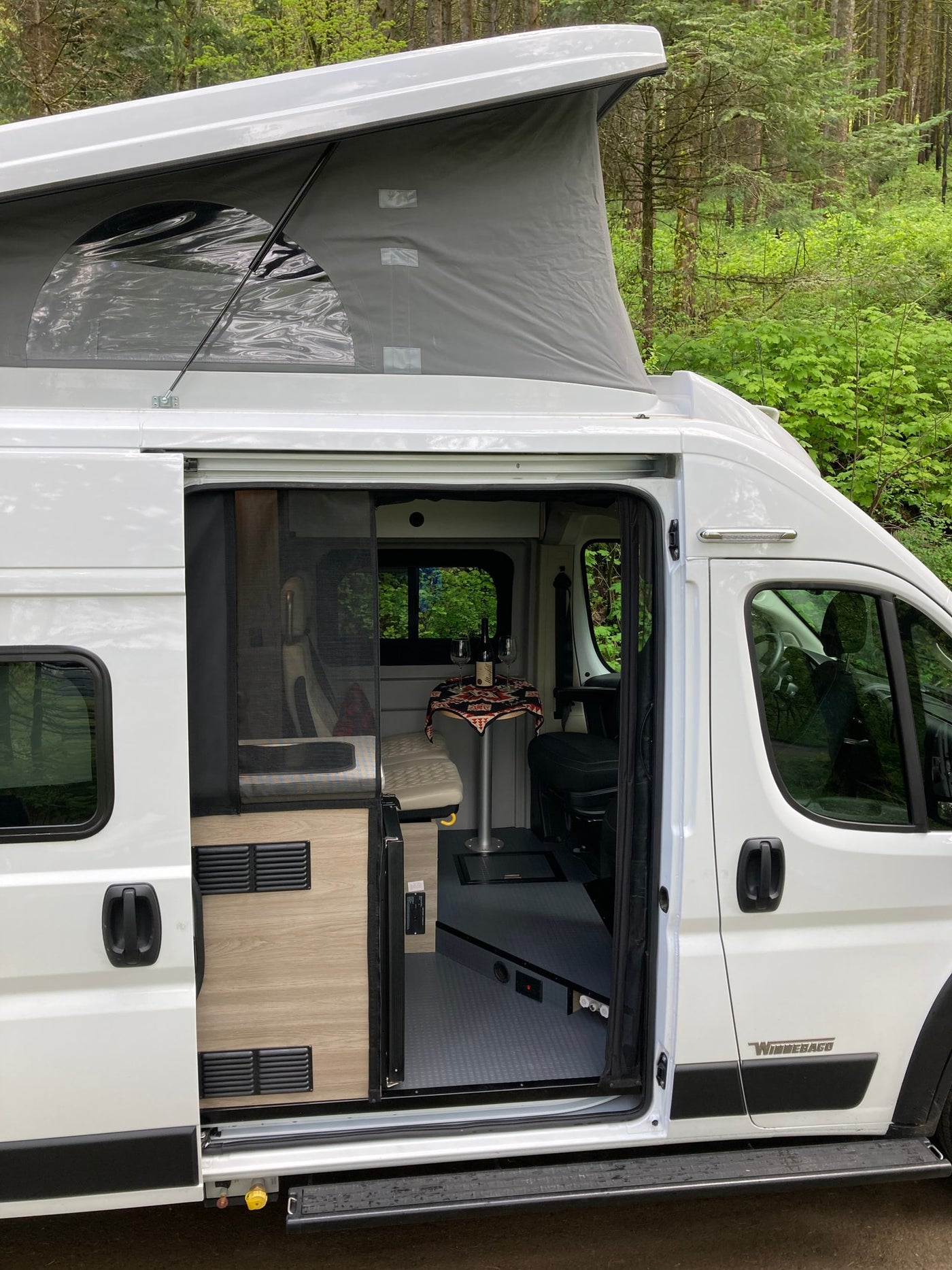  chairs and fire pit nearby.|White Winnebago Solis RV rental camper van with pop-top open — photo 12