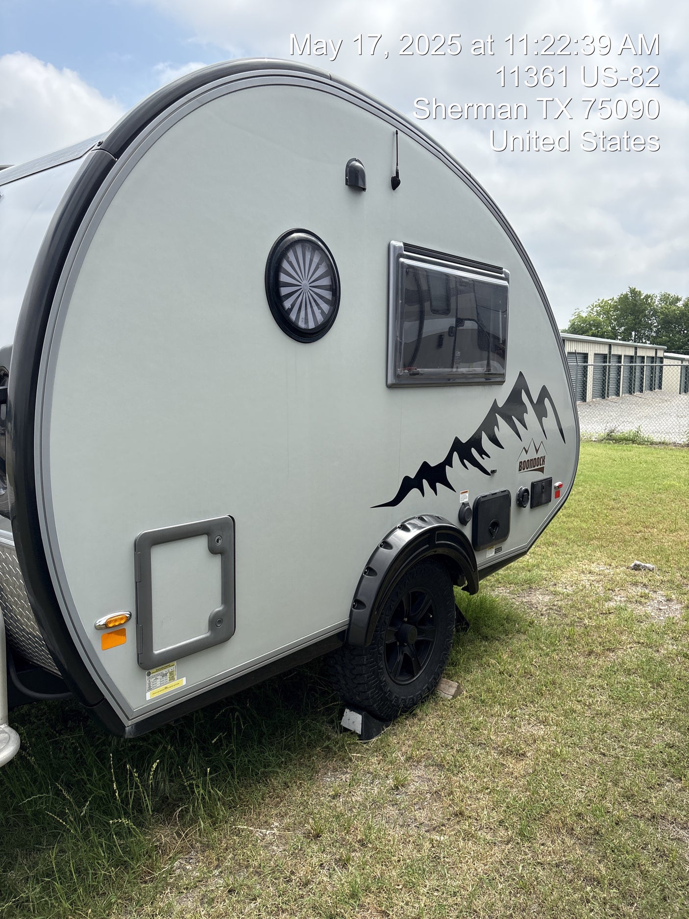 A gray Boondock teardrop RV, possibly an RV rental, parked on grass near storage units in Sherman, TX.