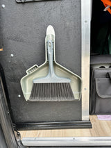Compact grey dustpan and brush neatly mounted on a textured wall in an RV rental for easy cleanup.