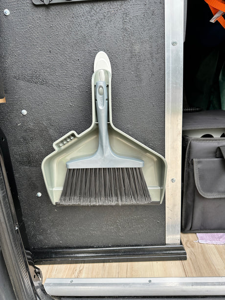 Compact grey dustpan and brush neatly mounted on a textured wall in an RV rental for easy cleanup.