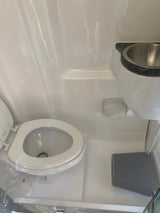 Compact rv rental bathroom featuring a white toilet with open lid, overhead sink, and hanging storage bin.