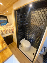 Compact RV rental interior with a chic hexagon-tiled shower/toilet and a comfortable bed