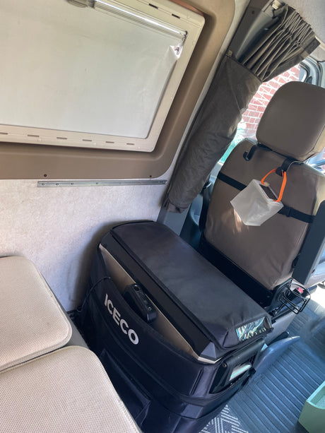 Compact RV rental interior: ICECO portable fridge, passenger seat with LuminAID light, and window curtains for travel comfort.