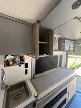 Inside this RV rental: a compact kitchen with a sink, comfortable bench seating, and smart overhead storage including bins.