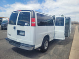 White Chevrolet van with open side doors on an asphalt lot. An RV is visible nearby, ideal for rv rental pickup.