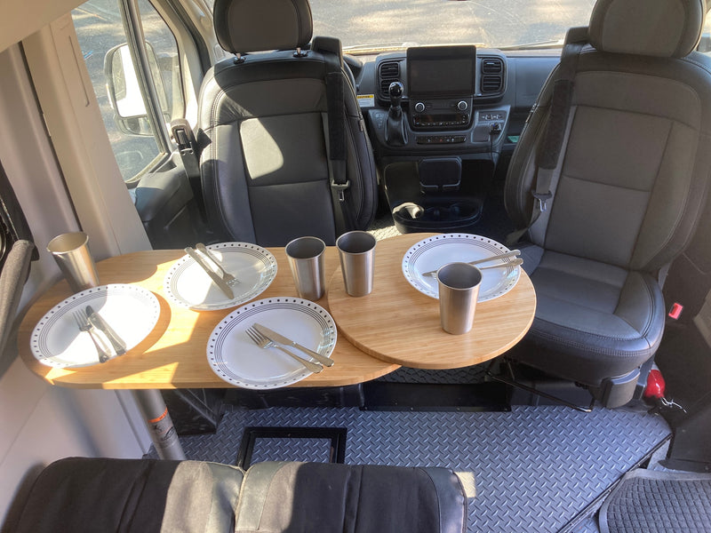 Interior of an RV rental, featuring swiveling front seats, dashboard, and a wooden dining table set with plates and cups. Diamond plate floor. — photo 11