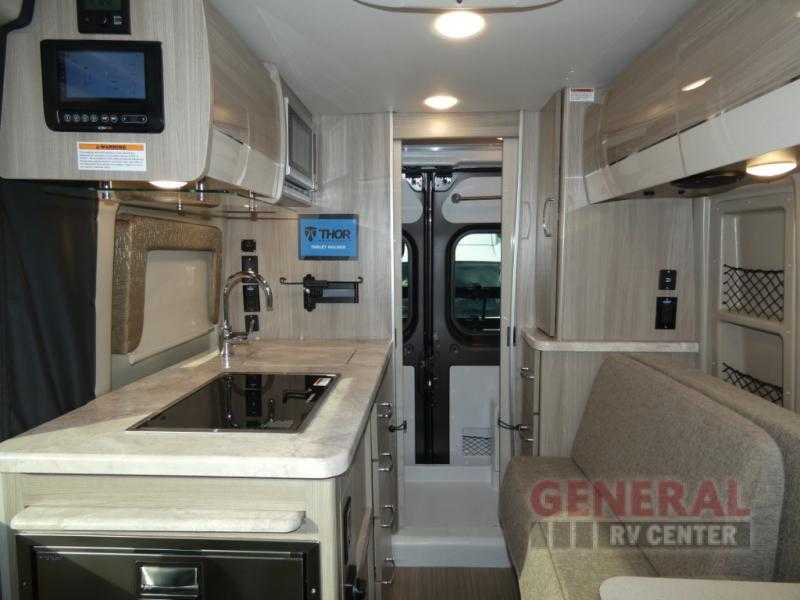 Modern RV rental interior: a compact kitchen with sink/stovetop, integrated control panel, and comfortable lounge seating visible. — photo 10