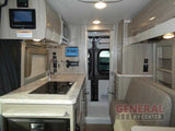 Modern RV rental interior: a compact kitchen with sink/stovetop, integrated control panel, and comfortable lounge seating visible.