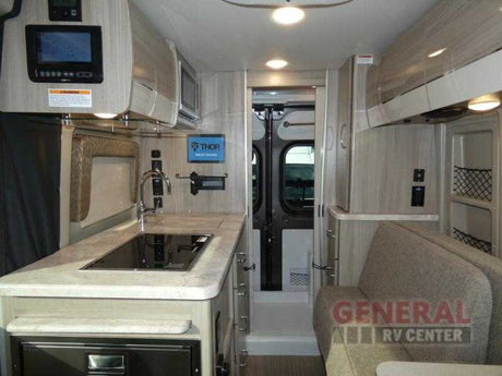 Modern RV rental interior: a compact kitchen with sink/stovetop, integrated control panel, and comfortable lounge seating visible.