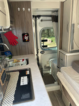 Compact RV rental interior featuring a kitchen with Dometic stove, sink, an adjacent wet bath, and seating/sleeping area.