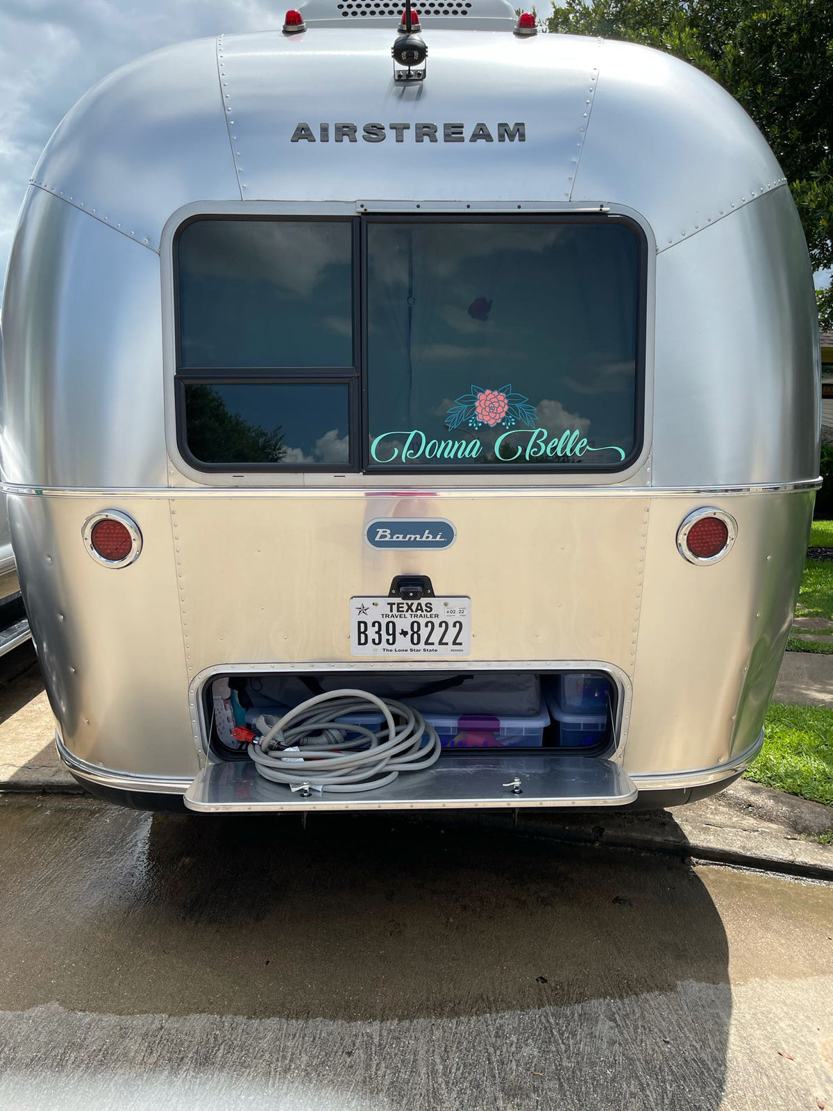 Rear view of a shiny silver Airstream Bambi travel trailer, "Donna Belle," with open storage, perfect for RV rental. — photo 7