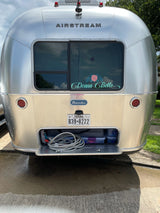 Rear view of a shiny silver Airstream Bambi travel trailer, "Donna Belle," with open storage, perfect for RV rental.