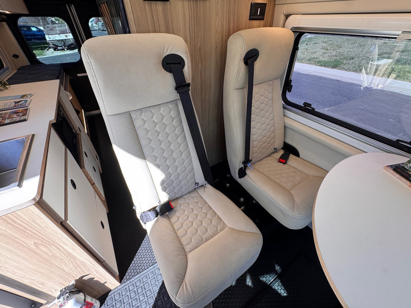 Bright rv rental interior featuring two comfortable passenger seats with seatbelts, a small table, and a compact kitchen. — photo 11