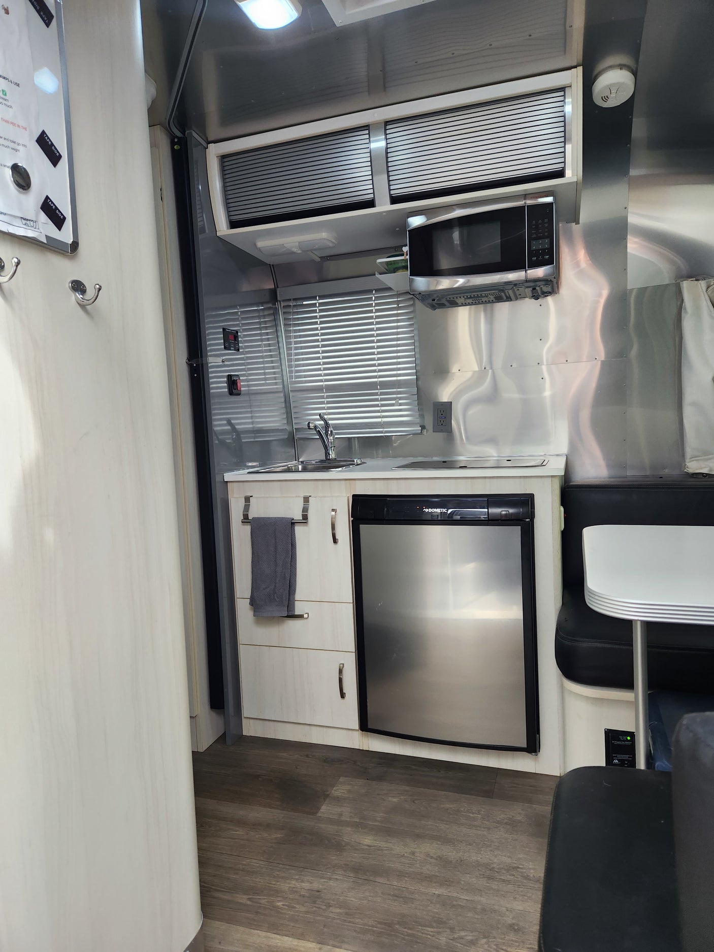 Inside an RV rental, a compact kitchen with a microwave, sink, refrigerator, and small dining booth.