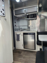 Inside an RV rental, a compact kitchen with a microwave, sink, refrigerator, and small dining booth.