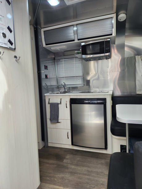Inside an RV rental, a compact kitchen with a microwave, sink, refrigerator, and small dining booth.