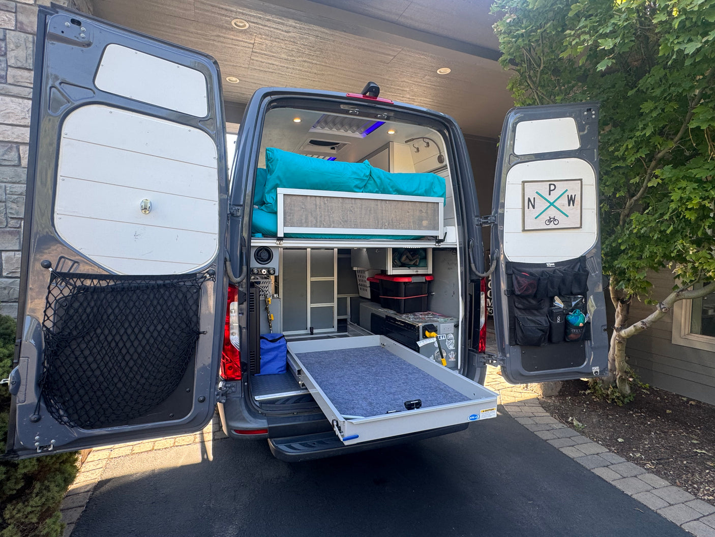Adventure-ready RV rental camper van showcasing an organized interior with a bed and pull-out storage.