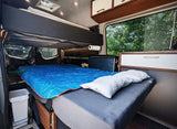 This RV rental offers a spacious interior: main bed with blue sleeping bag, an upper bunk, and ample storage.