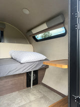 Cozy rv rental interior: a bed with a pillow, window view, ceiling light, and a small wooden side table.