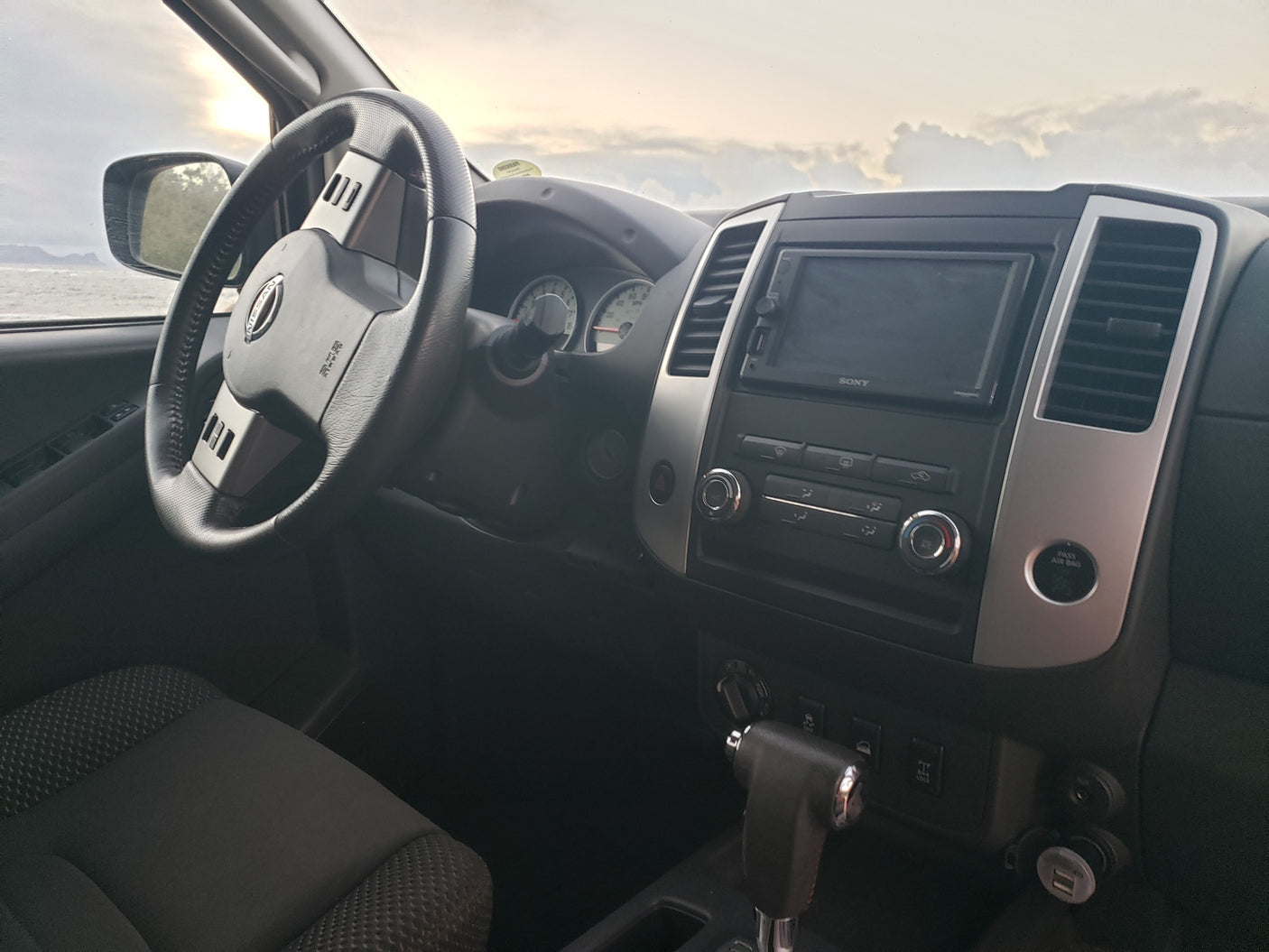 Inside a Nissan SUV: driver's view of steering wheel, dashboard, and a beach outside. Great for a road trip or an RV rental adventure.
