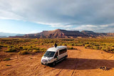 Enjoying the breathtaking desert landscape from atop an RV rental van, with majestic red rock mountains in the distance.