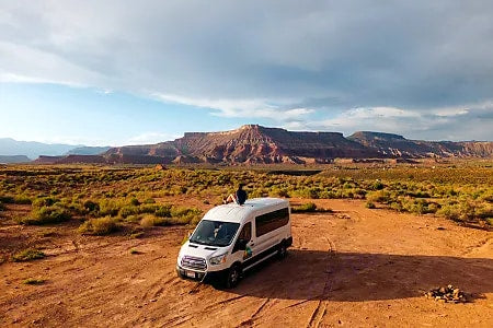 Enjoying the breathtaking desert landscape from atop an RV rental van, with majestic red rock mountains in the distance.