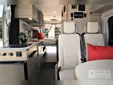 This modern RV rental interior features a bright living space with a kitchen, seating, and bed for comfortable travel.