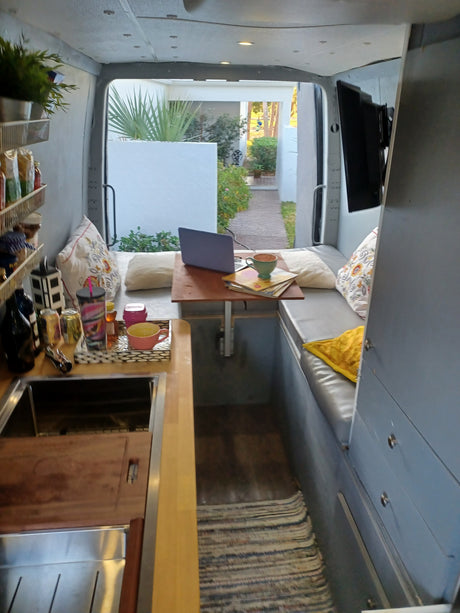 Cozy RV rental interior: compact kitchenette, comfy seating with laptop & magazines, plus a refreshing outdoor view.