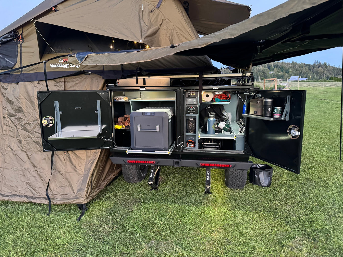 Adventure-ready RV rental setup: an open outdoor kitchen with portable fridge, organized storage, and a deployed rooftop tent. — photo 5