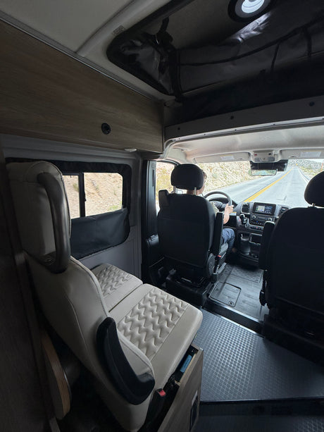 Interior view of an rv rental camper van on a desert road trip. Driver at the wheel, comfortable passenger seating visible.
