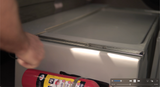 A red fire extinguisher is securely placed inside an RV rental, with a hand visible, highlighting essential safety equipment.