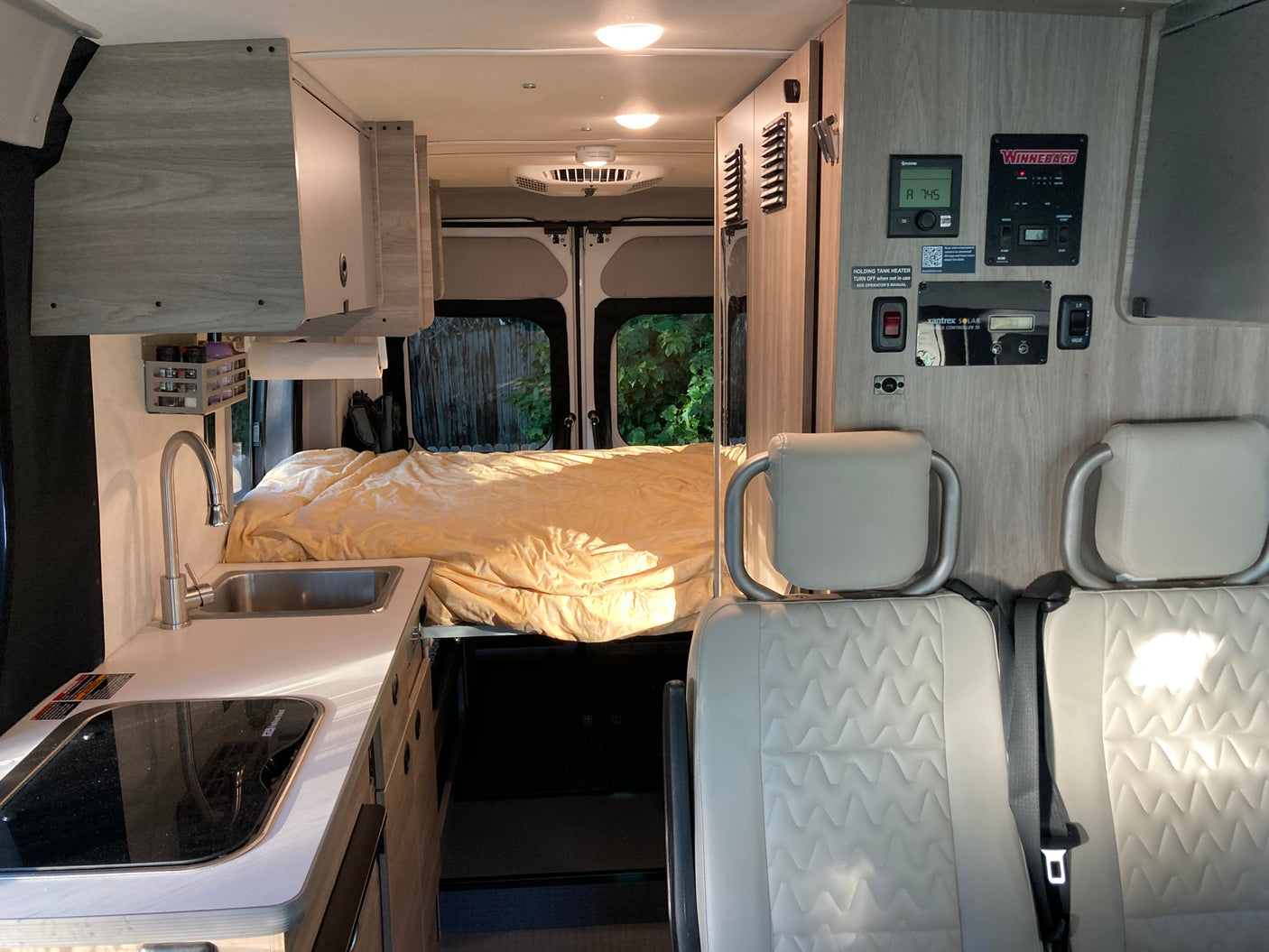 Modern Winnebago RV rental interior: galley, bed, and passenger seating, with visible control panels. Perfect mobile adventure.