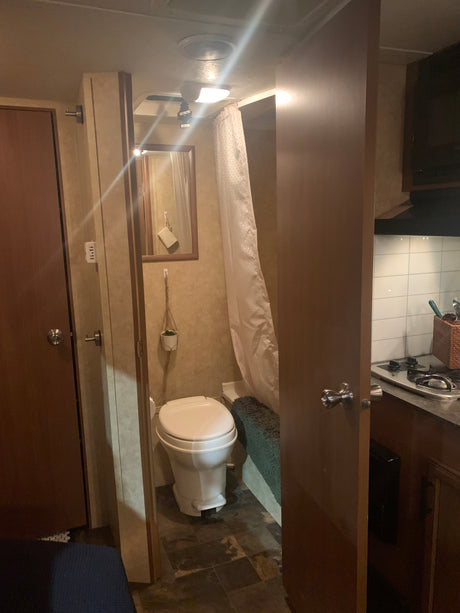Compact RV rental interior featuring a bathroom with toilet & shower, and a kitchen with stove.