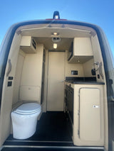 RV rental: Compact camper van interior featuring a toilet, kitchen with microwave, and bright cabinetry, designed for road trip comfort.