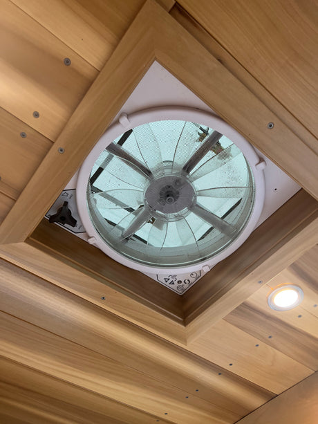 RV rental ceiling: a functional fan/vent with a mesh screen, framed by warm wood paneling, plus a bright LED light.