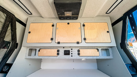 Compact RV rental interior with integrated storage cabinets, intuitive control panel, and overhead AC. Efficient design for travel.