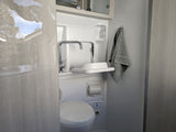 Compact RV rental wet bath, featuring toilet, sink, faucet, and towel. Includes light & fan controls.