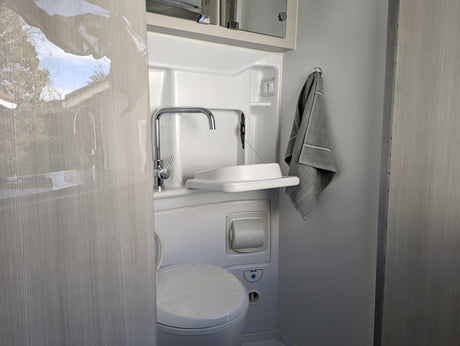Compact RV rental wet bath, featuring toilet, sink, faucet, and towel. Includes light & fan controls.