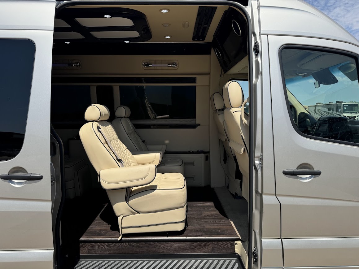 Luxury **rv rental** van interior with cream leather captain's chairs, wood floor, and custom overhead lighting. — photo 6
