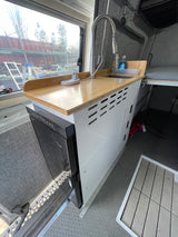 RV rental interior showing a modern kitchenette with a wooden countertop, sink, and built-in refrigerator.